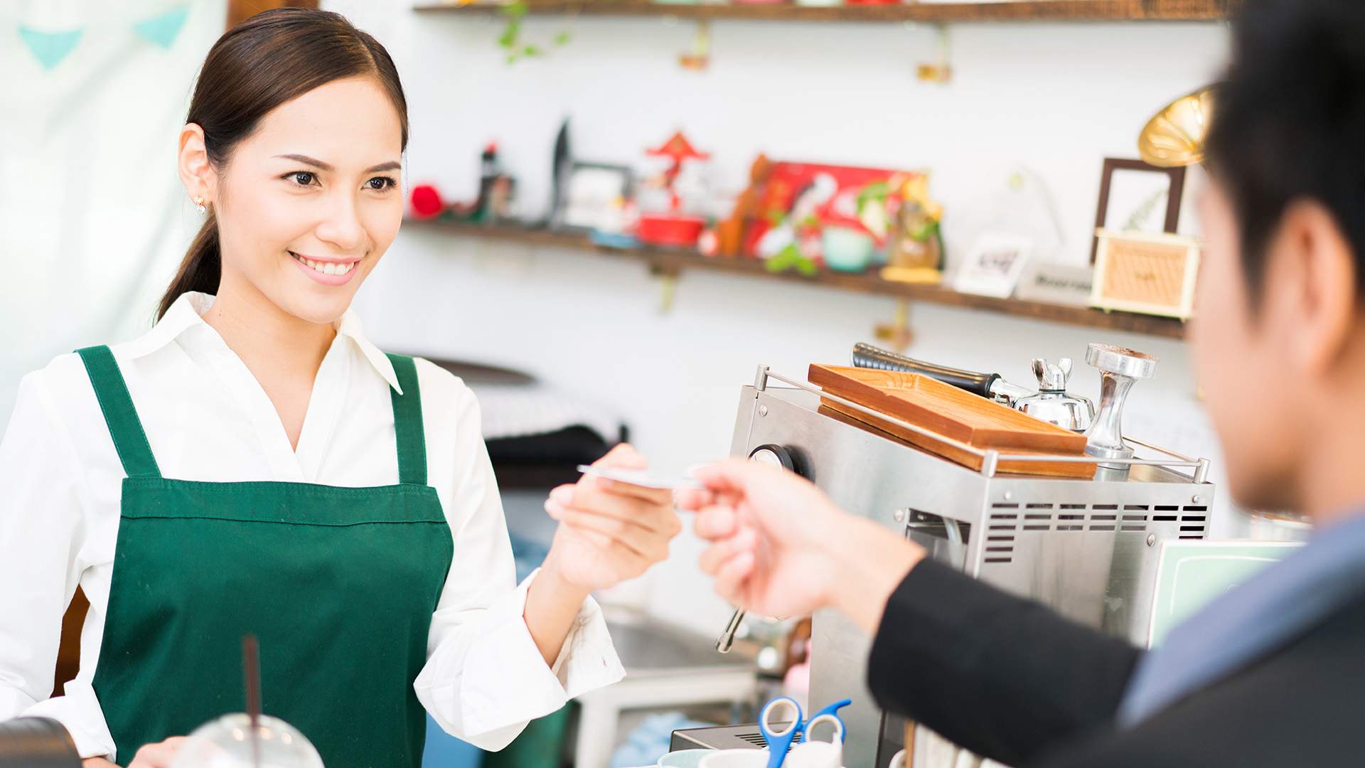 Barista is making coffee at his restaurant. and own a coffee shop she is swiping credit card. Where customers are paying